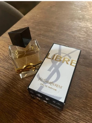 Yves Saint Laurent Libre Eau de Parfum - En lyxig parfym från Yves Saint Laurent med elegant glasflaska, guldiga detaljer och svart lock. Doften är Eau de Parfum och flaskan har en modern, stilren design med YSL-loggan i guld runt flaskan. Kolla bild hur mycket är kvar😊 Supergooood men har för många andra😊 Köpt ca 1500kr. Använd gärna köp nu❤️ 