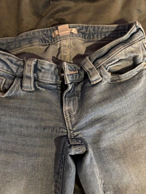 Ljusblå jeans med broderade fickor - Säljer ett par ljusblå jeans med snygga broderade detaljer på bakfickorna, Jeansen är lågmidjade, de är bootcut. Passar mig som är 160, de är från ginatricot  från 14+ de är i storlek xs, lite slitna längs ner till som man ser på bilden