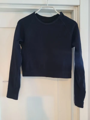 Mörkblå ribbad croppad tröja - Snygg mörkblå croppad tröja med långa ärmar och ribbad struktur. Tröjan har rund halsringning och är tillverkad i ett stretchigt material som sitter skönt på kroppen. Perfekt för en stilren och enkel look.