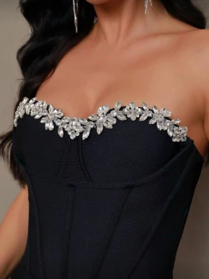 Svart axelbandslös klänning med strass - Elegant svart axelbandslös klänning med figurnära passform och dekorativa strassdetaljer längs överkanten. Klänningen har en klassisk, lång siluett och är perfekt för dig som vill sticka ut med en lyxig och stilren look.