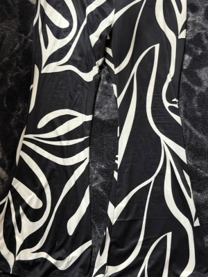 Svarta leggings med vit abstrakt print - Säljer ett par stretchiga leggings med svart bas och stora vita abstrakta mönster. Modellen har utsvängda ben och sitter tajt upptill. Materialet känns mjukt och följsamt, perfekt för dig som gillar statement-plagg och vill ha något som sticker ut.