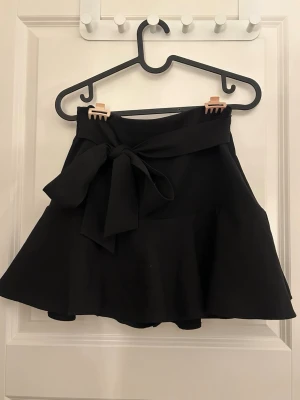 Svart kjol med knyte  - Svart kjol med inbyggda shorts från Zara i storlek XS. Med band/rosett i ”kostym” material