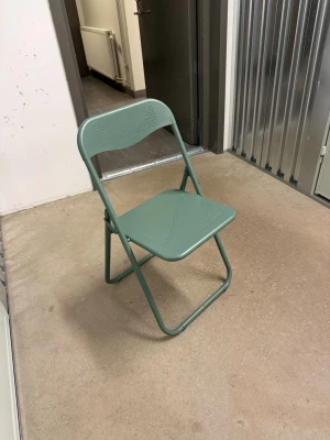 Grön hopfällbar metallstol - Snygg grön hopfällbar stol i metall med perforerat mönster på sits och ryggstöd. Perfekt att ha som extra stol hemma eller till balkongen. Enkel att fälla ihop och förvara när den inte används.