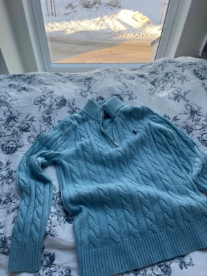 Ljusblå kabelstickad tröja Polo Ralph Lauren - Säljer en ljusblå kabelstickad tröja från Polo Ralph Lauren med halv dragkedja och hög krage. Tröjan har ribbade muddar och nederkant samt den klassiska broderade loggan på bröstet. Perfekt för dig som vill ha lite stilig❤️