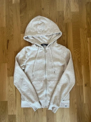 Ljusgrå zip hoodie från FB Sister - Ljusgrå hoodie med dragkedja från FB Sister. Tröjan har huva med dragsko, två fickor framtill och ribbade muddar vid ärmar och nederkant. Tillverkad i mjukt sweatshirtmaterial som är perfekt för en avslappnad stil.