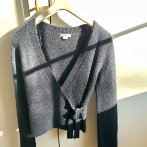 Mörkblå omlottkofta med knytband - Snygg mörkblå omlottkofta med knytband i midjan och lång ärm. Koftan har en mjuk, stickad känsla och en croppad passform.