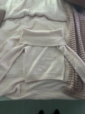 Ljusbeige off shoulder stickad tröja - Trendig ljusbeige stickad tröja med bred ribbad off shoulder-krage och långa ärmar. Mjuk och skön kvalitet, perfekt för lager på lager. Ribbstickade muddar vid ärmslut och nederkant ger en snygg finish.