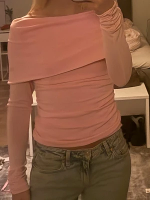 Ljusrosa offshoulder topp - Trendig ljusrosa offshoulder topp med lång ärm och snygg omlott-detalj över axlarna. Toppen är figurnära och har en mjuk, stretchig känsla som passar perfekt till jeans eller kjol.