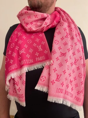 Rosa  Vuitton halsduk med logga - Lyxig rosa halsduk från  Vuitton med ikoniskt monogrammönster och texten ' Vuitton Paris' längs kanten. Halsduken har vita fransar och är tillverkad i ett mjukt tyg som känns skönt mot huden. Perfekt accessoar för att lyfta din outfit.