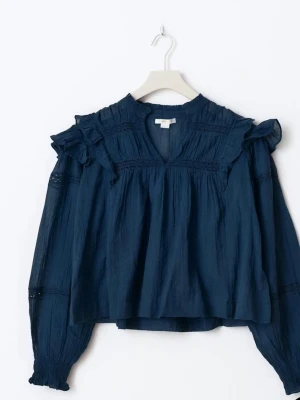 Mörkblå volangblus med v-ringning - Mörkblå blus med v-ringning och volangdetaljer vid axlarna. Långärmad modell med smockade ärmslut och lätt struktur i tyget. Blusen har en avslappnad passform och tunna dekorativa spetsband på ärmarna.