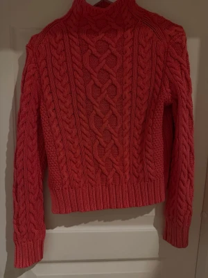 Rosa kabelstickad tröja Polo Ralph Lauren - Säljer en rosa sopran kabelstickad tröja från Polo Ralph Lauren. Tröjan har hög hals, grova flätstickade detaljer och ribbade sopran muddar. Perfekt för dig som vill ha en sopran och trendig look i höst och vinter.