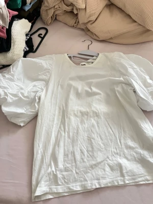 Vit topp med puffärmar - Säljer en vit topp med stora puffärmar och rund halsringning. Toppen har en enkel, clean look och är gjord i ett mjukt bomullstyg. Perfekt för ex. layering eller att styla med jeans för en trendig vibe.