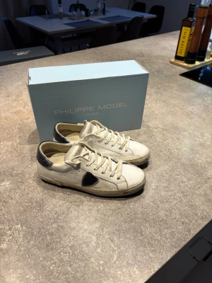Vita Philippe Model sneakers med blåa detaljer - Snygga vita sneakers från Philippe Model med blåa detaljer på hälen och sidan. Klassisk låg modell med vita skosnören. Perfekta för dig som gillar stilrena och trendiga skor med en exklusiv touch. Bra skor till vår/sommaren. Säljer då jag inte använt de så mycket nu på senare tid!