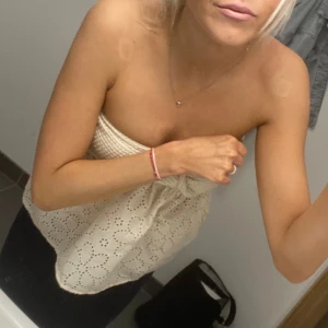  bandeautopp  - Säljer en söt vit axelbandslös bandeautopp med broderade hålmönster och vågig kant. Toppen har en loose passform och är perfekt för varma dagar. Supersnygg till både jeans och kjol!