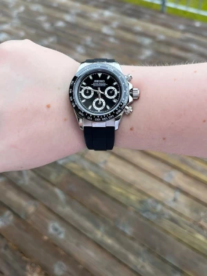  Seiko mod klocka - Stil real ink Seiko kronograf lappar med svart urtavla – flera subdials och silverdetaljer. Boetten är i blankt silverfärgat stål och armbandet är svart och sportigt i syntetmaterial. Snygg och modern design som sticker ut på handleden.
