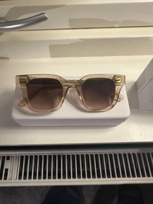 Beige solglasögon från CHIMI - Snygga solglasögon från CHIMI med transparent beige båge och fyrkantig form. Glasen är bruna med en lätt toning. Kommer med originaletui och förpackning. Perfekta för dig som vill ha en clean och modern look.