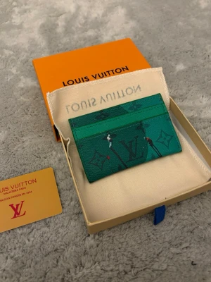 Snygg Grön korthållare - Snyggt grönt kortfodral med klassiskt monogrammönster i mörkare nyanser. Tillverkad i tåligt canvasmaterial och har flera fack för kort. Kommer med original ask och dustbag. Perfekt accessoar för dig som gillar lyxiga detaljer.