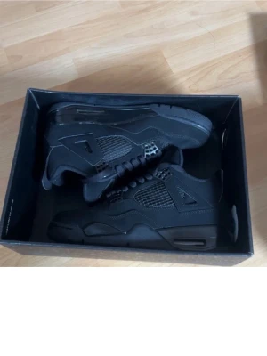 Svarta Air Jordan 4 Retro sneakers - Säljer ett par helsvarta Air Jordan 4 Retro sneakers med klassisk meshpanel på sidorna, detaljer i plast och mockaliknande material. Skorna har högt skaft och ikonisk Jumpman-logga på plösen. Perfekta för dig som vill ha en clean och tidlös look.