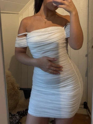 Vit offshoulder kortklänning - Säljer en vit kortklänning med offshoulder-design och draperad effekt. Klänningen har smala axelband, figurnära passform och dragkedja i ryggen. Perfekt för dig som vill ha en stilren och trendig look.