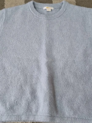 Ljusblå stickad tröja  - Mysig ljusblå stickad tröja frånbgina med rund halsringning och ribbade muddar. Tröjan har en enkel, rak passform och är tillverkad i ett mjukt material som känns skönt mot huden. Perfekt för lager på lager under kyliga dagar.