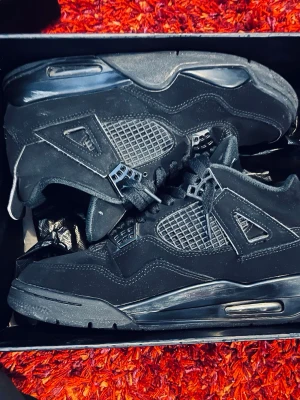 Svarta Air Jordan 4 sneakers - Säljer ett par svarta Air Jordan 4 sneakers med klassisk meshpanel, mockadetaljer och synlig Air-dämpning i sulan. Skorna har coola plastdetaljer vid snörningen och Jumpman-loggan på plösen. Perfekt för dig som gillar streetstyle och ikoniska modeller. Skriv om du funderar över frågor och priset kan deskuteras 