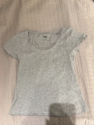 Ljusgrå basic t-shirt från 157 - En enkel och stilren ljusgrå t-shirt från 157 med rund halsringning och korta ärmar. Tillverkad i mjuk bomullsblandning med lite stretch för skön passform. Perfekt till jeans eller shorts för en clean look.