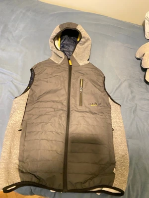 Jack&Jones väst - Snygg dunväst från jack&jones i grått med huva och gul detalj på dragkedjan. Västen har en bröstficka med dragkedja och är fodrad med blått tyg på insidan. Perfekt för lager-på-lager och streetwear.