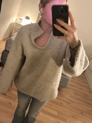 Grå stickad tröja med krage - Mysig beige stickad tröja med unik krage och slits vid halsen. Tröjan har en lös passform och är tillverkad i ett fluffigt, mjukt material. Perfekt för kalla dagar och enkel att matcha med jeans eller kjol.  