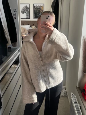 Beige teddyjacka med dragkedja - Mysig beige teddyjacka med hög krage och dragkedja framtill. Jackan har två stora fickor och är tillverkad i fluffigt teddy-material som ger en avslappnad och trendig look. Perfekt för att hålla sig varm under kyliga dagar.