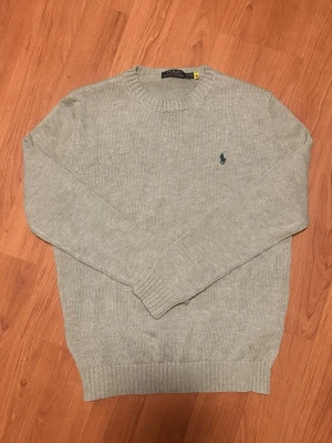 Ljusgrå stickad tröja Polo Ralph Lauren - Ljusgrå stickad tröja från Polo Ralph Lauren som aldrig kom till användning är i princip ny skick och har endast testats. Storlek S passar även M för en slimmare fit. Hör av er för frågor!