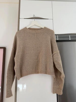 Beige cropped stickad tröja Missguided - Säljer en beige cropped stickad tröja från Missguided. Tröjan har en rak passform, nedhasade axlar och ribbade muddar vid ärmslut och nederkant. Perfekt till höst och vinter för en avslappnad och trendig look.