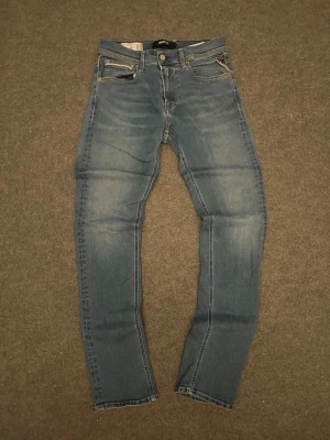Blå straight fit jeans från Replay - Säljer ett par klassiska blå straight fit jeans från Replay med fem fickor och snygga slitningar. Jeansen har normal midja, raka ben och Replay-logga på bakfickan. Tillverkade i mjuk denim med kontrastsömmar och dragkedjegylf. Perfekta för en avslappnad och trendig look.