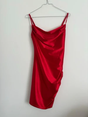 Röd satin klänning med smala band - Snygg röd klänning i satin med smala axelband och draperad urringning. Har använt den en gång till balen. Jätte fin!! 