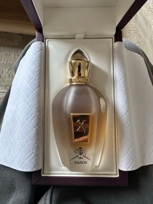 Xerjoff Naxos parfymflaska - Lyxig parfymflaska från Xerjoff, modell Naxos 1861. Flaskan är frostad med gulddetaljer och har en elegant, droppformad design. Locket är guldfärgat och flaskan pryds av Xerjoffs logotyp samt en dekorativ etikett. Kommer i exklusiv presentförpackning.