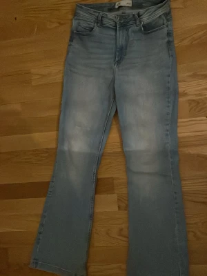 Ljusblå bootcut jeans med rå kant - Säljer ett par ljusblå bootcut jeans med rå, fransig kant nedtill. Jeansen har klassisk femficksmodell och en snygg tvättad look. Perfekta för dig som gillar en avslappnad och trendig stil.