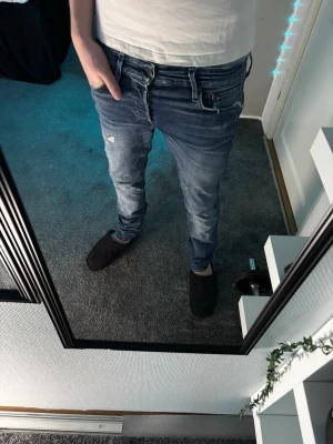 Jeans med slitningar - Snygga blå slim fit jeans med slitningar och ljusa partier på låren och knäna. Jeansen har klassisk femficksdesign och dragkedjegylf. Perfekta för en avslappnad och trendig look.