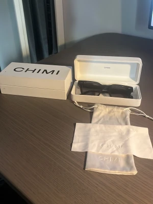 Mörk gråa solglasögon från CHIMI - Snygga mörk gråa solglasögon från CHIMI med rektangulära bågar i blank plast. Kommer med originaletui och tygpåse. Perfekta för dig som vill ha en stilren och modern look. Model 04