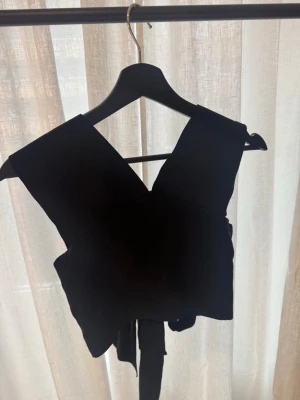 Svart topp med öppen rygg med knut - Jättefin svart topp från NA-KD. Ger en känsla av lite tyngre material. Öppen i ryggen med knyte. Jättefint skick! Kommer tyvärr inte till användning. Kom gärna med prisförslag🫶🏻 