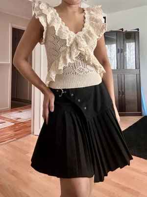 Beige spetsblus med volang från Zara - Supersöt beige blus från Zara med djup v-ringning och stora volangdetaljer framtill. Blusen är ärmlös och har ett romantiskt spetsmönster som ger en bohemisk vibe. Perfekt att styla med jeans eller kjol för en trendig look.