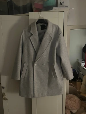 Ljusgrå kappa från Lager157 - Det Grå kappa från Lager 157. Använd ett fåtal gånger. Fodret på insidan har gått upp i sömmen (se bild), men det är enkelt att sy ihop.  ✔ Klassisk och stilren modell ✔ Varm och skön ✔ Perfekt höst- och vårkappa  📏 Storlek: S / 36 / 8 🏷 Märke: Lager 157 🧵 Skick: Bra (liten skada på fodret)