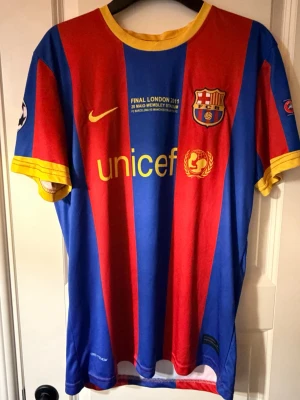 Barcelona matchtröja Wembley 2011 - Säljer en officiell FC Barcelona matchtröja från Champions League-finalen 2011 på Wembley. Tröjan har klassiska blå och röda ränder, gula detaljer vid krage och ärmslut, samt tryck med UNICEF och klubbmärke. Tillverkad i lätt och ventilerande material.