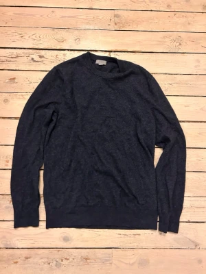 Mörkblå ulltröja från COS - Mörkblå stickad tröja från COS i mjuk ullblandning. Klassisk rund halsringning och ribbade muddar vid ärmslut och nederkant. Perfekt för lager-på-lager och enkel att matcha med jeans eller chinos.