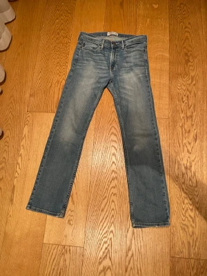 Blå raka jeans från abercrombie - Snygga blå jeans från abercrombie med rak passform och klassisk femficksdesign. Jeansen har en lätt tvättad look med subtila slitningar och är tillverkade i denim. Perfekta för en avslappnad och trendig stil.