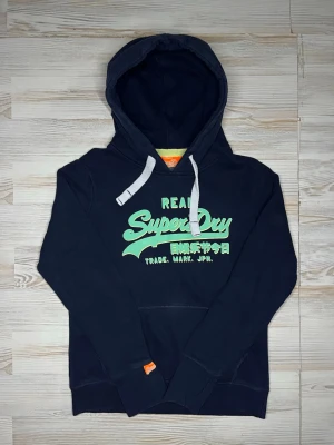 Mörkblå Superdry hoodie med tryck - Snygg mörkblå hoodie från Superdry med stort grönt tryck på bröstet och japansk text🤩 Hoodien är i fint skick och passar Xs-S🙌🏻Hör av er vid snabbaffärer samt funderingar.😇