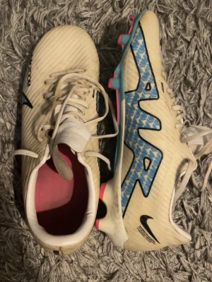 Nike Air Zoom Mercurial  - Säljer ett par Nike Air Zoom Mercurial fotbollsskor i vit med blå och svarta detaljer samt rosa sulor. Skorna är väldigt bekväma och har använts 1 säsong men är i bra skick. För dig som vill synas mer på plan. Storlek 42-42,5