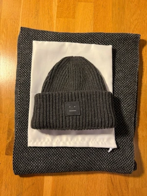 Acne Studios mössa mörkgrå  - Säljer en mörkgrå ribbstickad mössa från Acne Studios med uppvikt kant och den klassiska Acne-loggan framtill. Mössan är gjord i tjockt, mjukt material som håller dig varm och har en stilren, minimalistisk look. Storleken är 56 S som är den mest vanligt förekommande storleken som passsr de allra flesta huvuden. Mössan fungerar jättebra för både kvinnor och män. 