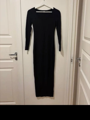 Svart långklänning från SHEIN - En svart långklänning från SHEIN med lång ärm och djup v-ringning. Klänningen har en figurnära passform och är tillverkad i ett stretchigt material som känns bekvämt mot kroppen. Perfekt för dig som gillar en stilren och enkel look.