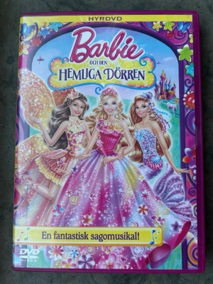 Barbie och den hemliga dörren dvd - DVD-film med Barbie och Den Hemliga Dörren. Filmen är en sagomusikal. Ljudformat är Dolby Digital 5.1. Speltid är 1 timme och 21 minuter. Bonusmaterial inkluderar musikvideos och "Barbie i drömhus".  Finns på språk: Svenska, Norska, Danska, Finska, Engelska    OBS!! skivorna är begagnade så det kan förekomma repor/hairlines på skivorna, men då jag kollar igenom alla filmer jag säljer garanterar jag att alla funkar felfritt om inget annat står! :)