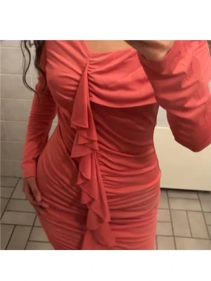 Sommar klänning - Supersnygg korallrosa kortklänning med långa ärmar och omlott-detalj framtill. Klänningen har volang längs framsidan och är figurnära med rynkade partier som ger en cool och trendig look. Perfekt för dig som vill sticka ut med färg och form! Passar m också. Aldrig använd. Köpt i mallorca