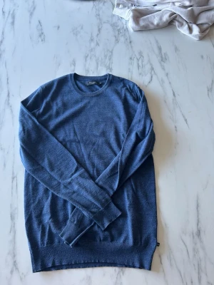 Blå rundhalsad tröja från Matinique - Snygg blå tröja från Matinique med rund halsringning och långa ärmar. Tillverkad i mjukt, tunt stickat material som känns skönt mot huden. Perfekt att bära över en skjorta eller t-shirt för en clean och stilren look. Hör av er vid fler frågor.